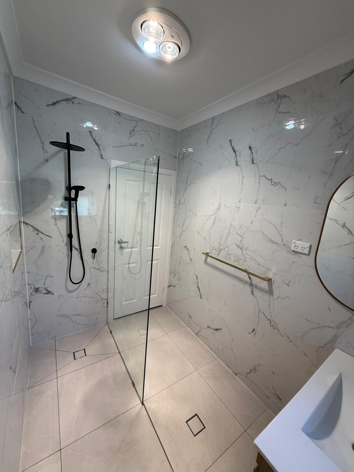 Full bathroom — marble walls, dual showers, gold towel bar